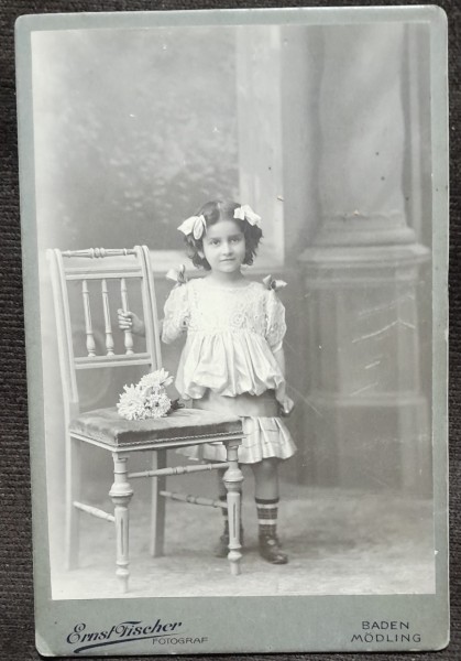 Fotografie pe carton, fetita cu fundite si buchet de flori, inceput de secol XX