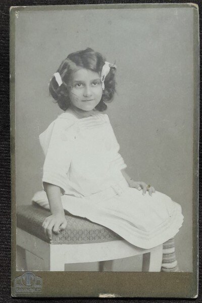 Fotografie pe carton, fetita cu fundite, stand pe scaun, inceput de secol XX