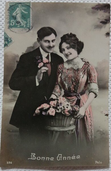 Fotografie tip Carte postala, barbat si femeie langa un cos cu flori, perioada interbelica