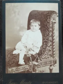Fotografie pe carton, copil asezat intr-un jilt, inceput de secol XX
