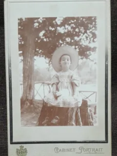 Fotografie pe carton, fetita la Slanic, asezata pe o bututuga, perioada interbelica