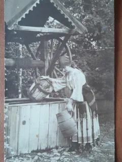 Fotografie tip carte postala, necirculata, tanara in port popular, sotand apa din fantana, inceput de secol XX